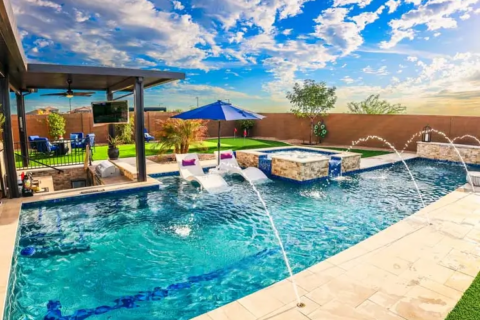 Luxurious backyard pool area in Phoenix, AZ, with a rectangular swimming pool, water jets, built-in lounge chairs, a hot tub with a waterfall feature, and a shaded seating area.