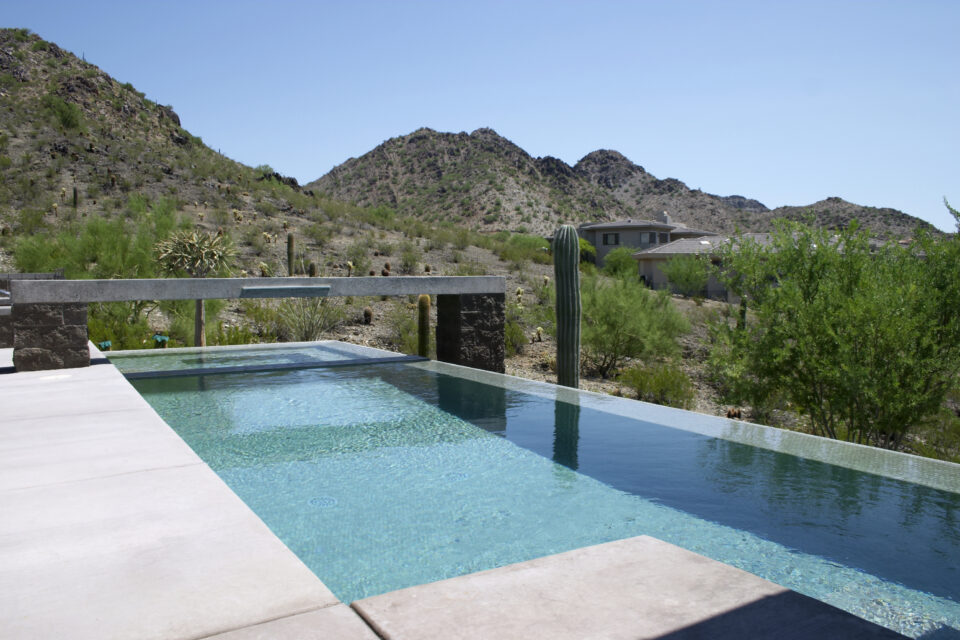 Infinity-edge pool with turquoise water overlooking a desert landscape, cacti, and mountains