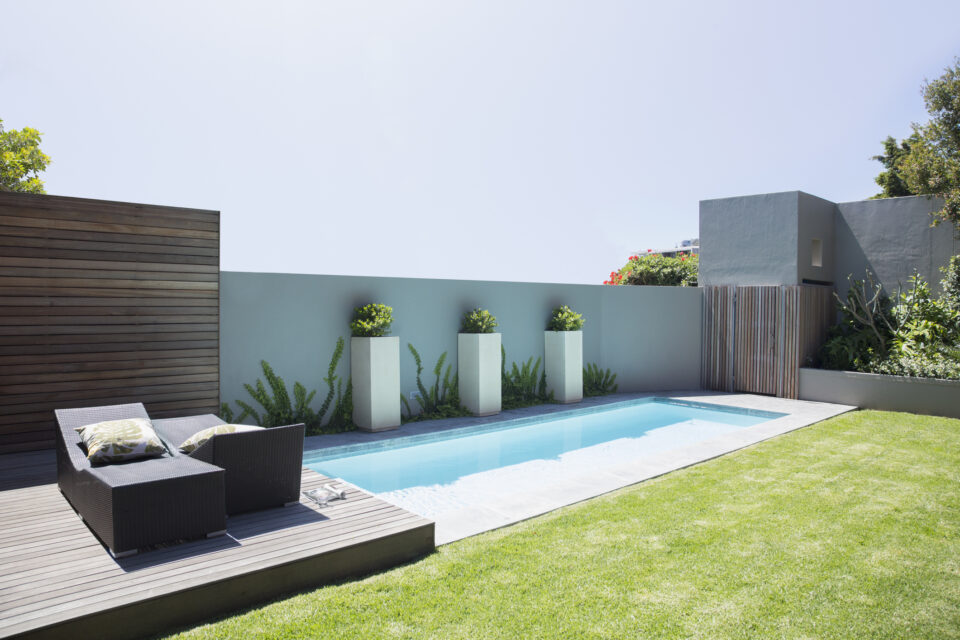 Lap pool with a sleek rectangular design, modern wooden decking, lounge chairs, and minimalist landscaping