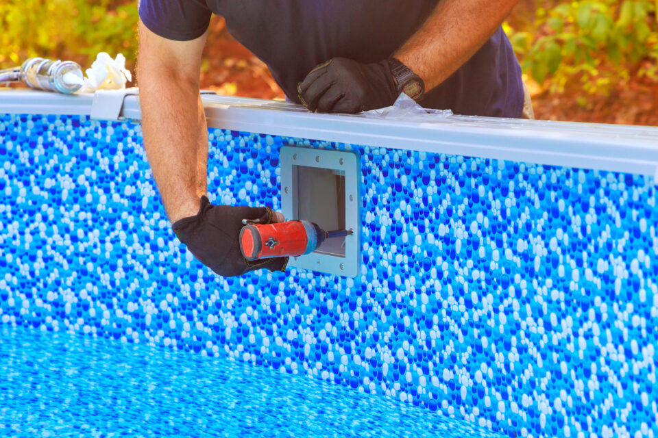 Installing a white fitting on an above-ground pool with a blue pebble-patterned liner during a new pool installation