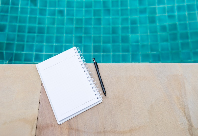 A notebook and pen placed on the poolside deck to make the swimming pool checklist in Phoenix, AZ